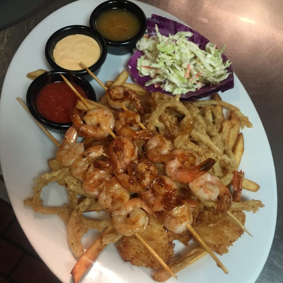 Shrimp skewers, french fries, onion rings, coleslaw, and three dipping sauces on a white plate.