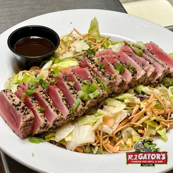 Seared tuna slices with sesame seeds and scallions, served over a fresh salad with dressing.