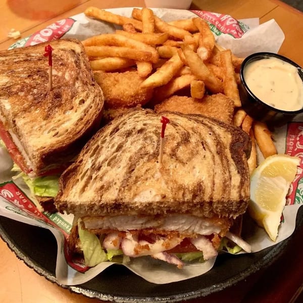 RJ Gator's fried fish sandwich on toasted bread with fries, hush puppies, tartar sauce, and lemon.