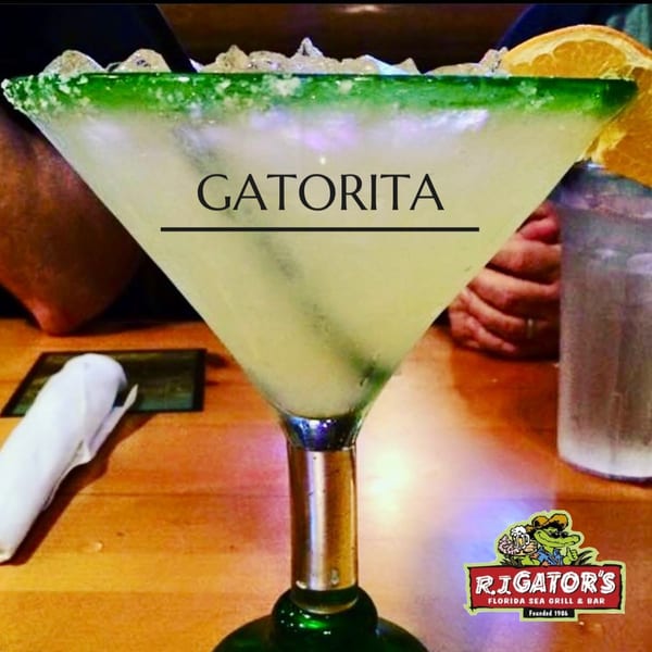 A Gatorita margarita in a salt-rimmed glass with an orange slice, on a wooden table.